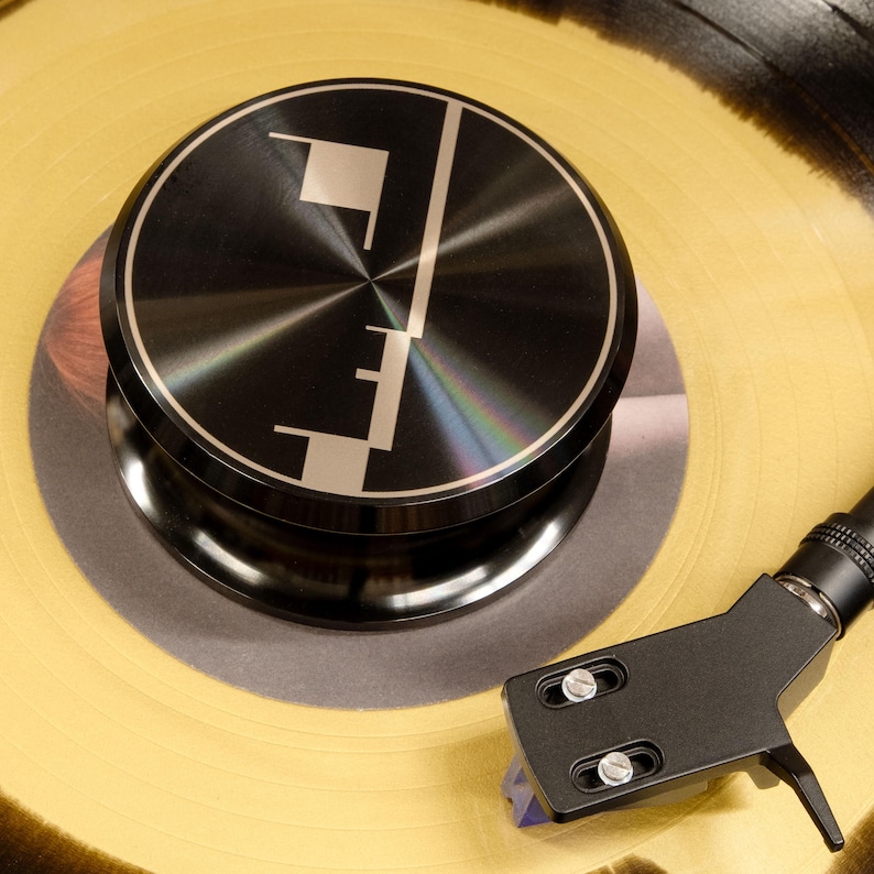 Geometric engraving on a black record weight resting on yellow vinyl